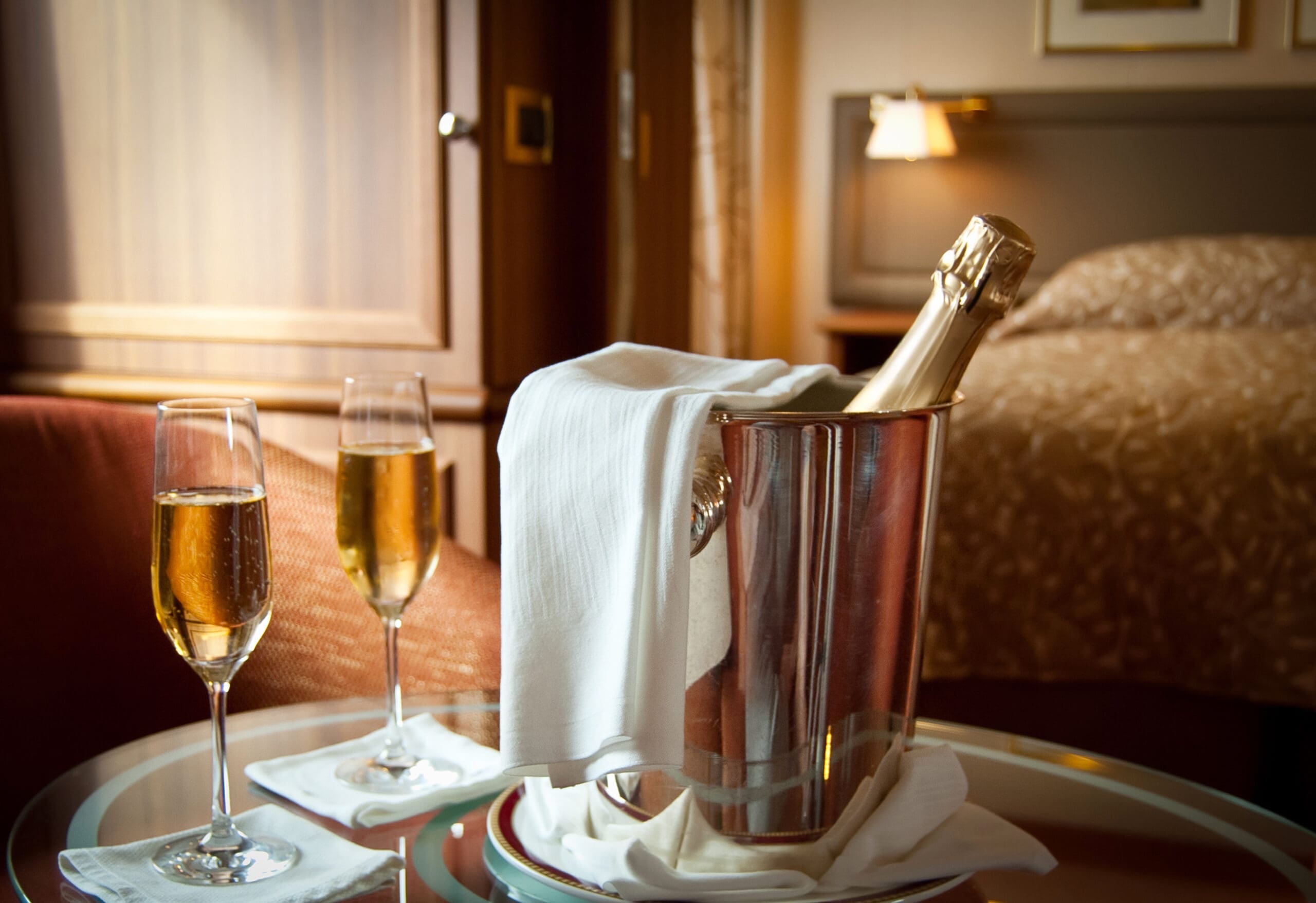 internal shot of hotel room with bottle of fizzy drink and two flutes filled with the same.